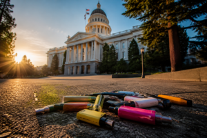 California State Capitol building with discarded disposable vapes in foreground illustrating AB 762 disposable vape ban legislation